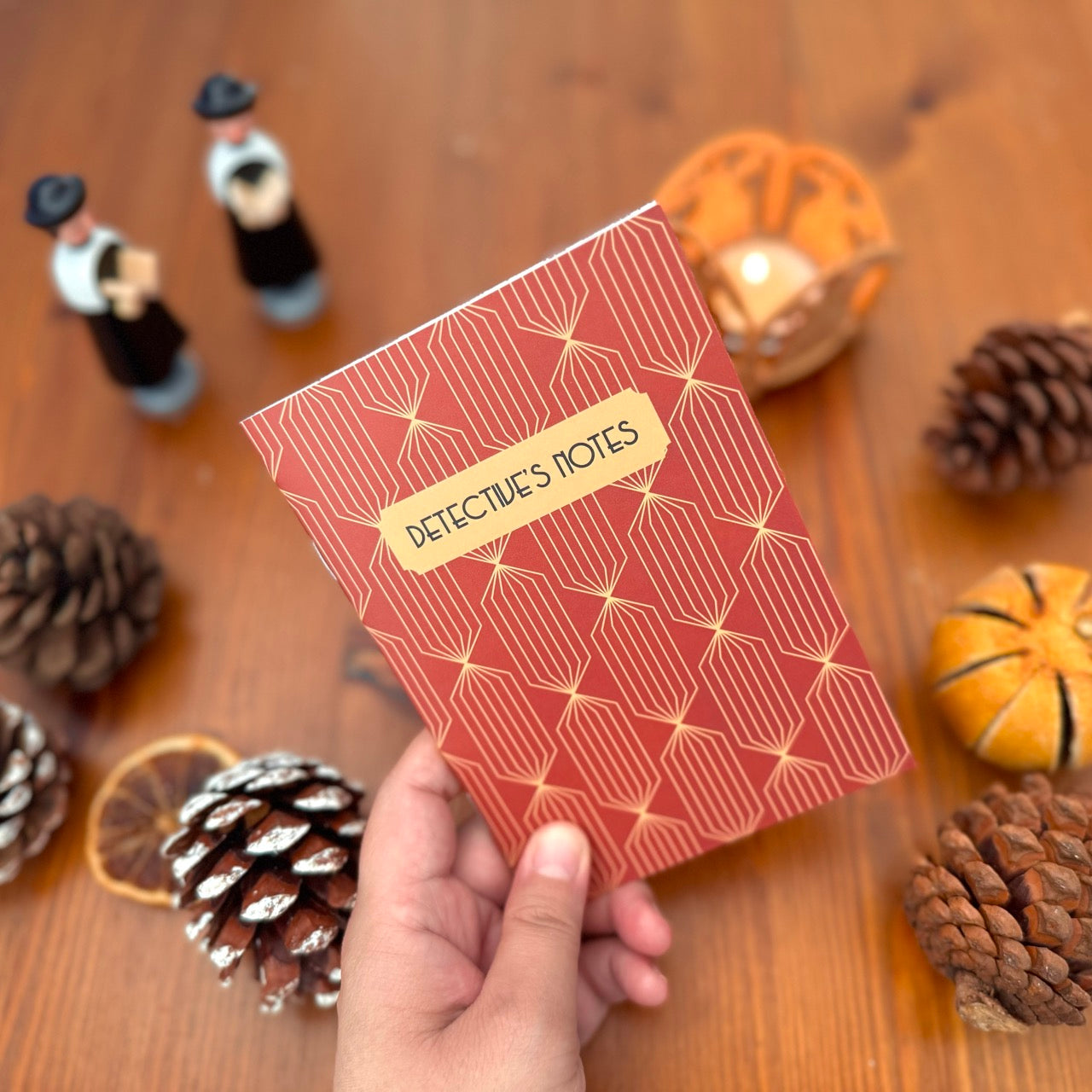 Notebook titled 'Detective's Notes' held by a hand on a wooden surface with decorative items.