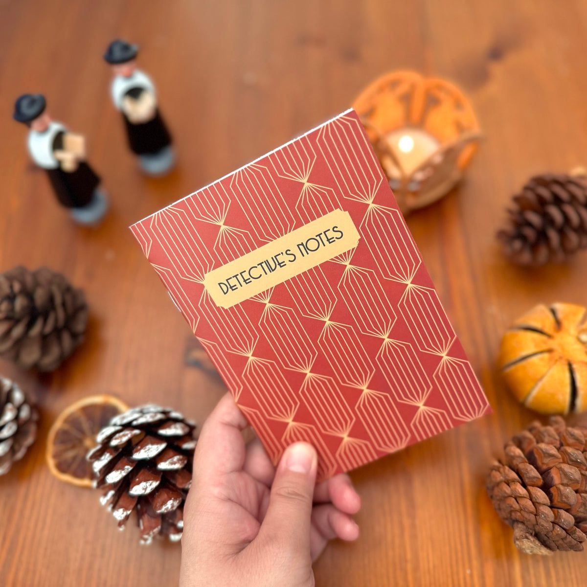 Notebook titled 'Detective's Notes' held by a hand on a wooden surface with decorative items.