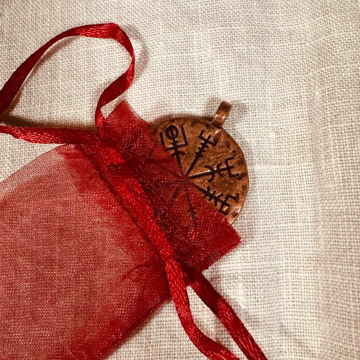 A round pendant with engraved runes and a red drawstring pouch.
